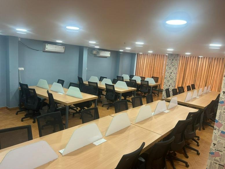 Open-plan office space at Mahatma Gandhi Road featuring multiple wooden desk rows and grey walls.