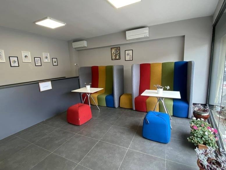 Colorful lounge area with rainbow-striped high-back seating booths and small white tables.