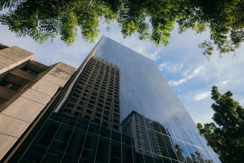 Low-angle view of the glass-facade 107 Aguirre building against a blue sky with clouds.