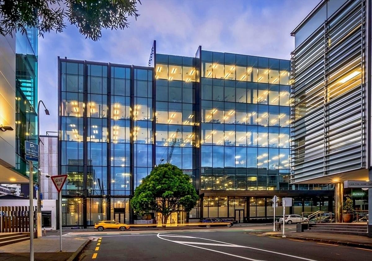 Exterior view of the multi-story glass building at 110 Carlton Gore Road with lit-up offices at dusk.