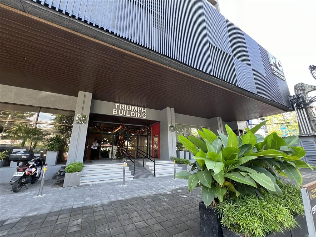 Modern entrance to the Triumph Building with lush green plants in the foreground.