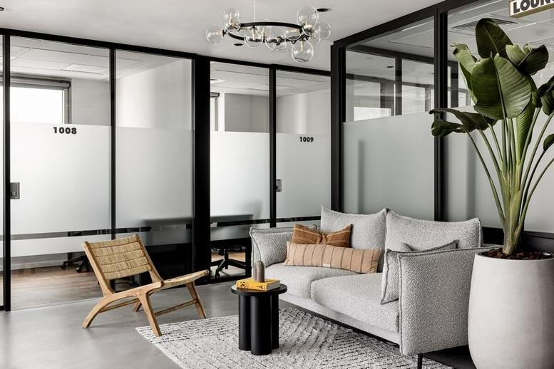 Modern lounge area with grey sofa, woven chair, and glass partitions at Millennium House.
