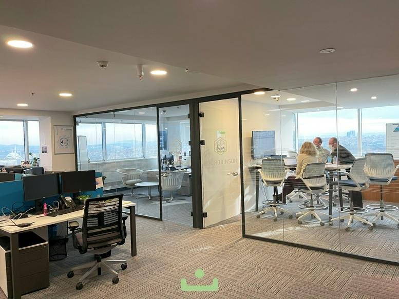 People in a glass-walled meeting room with high-top chairs and a monitor.