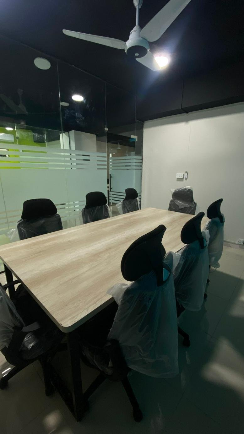 Meeting room at Talha Heights 2 with a light wood table, black chairs, and a white ceiling fan.