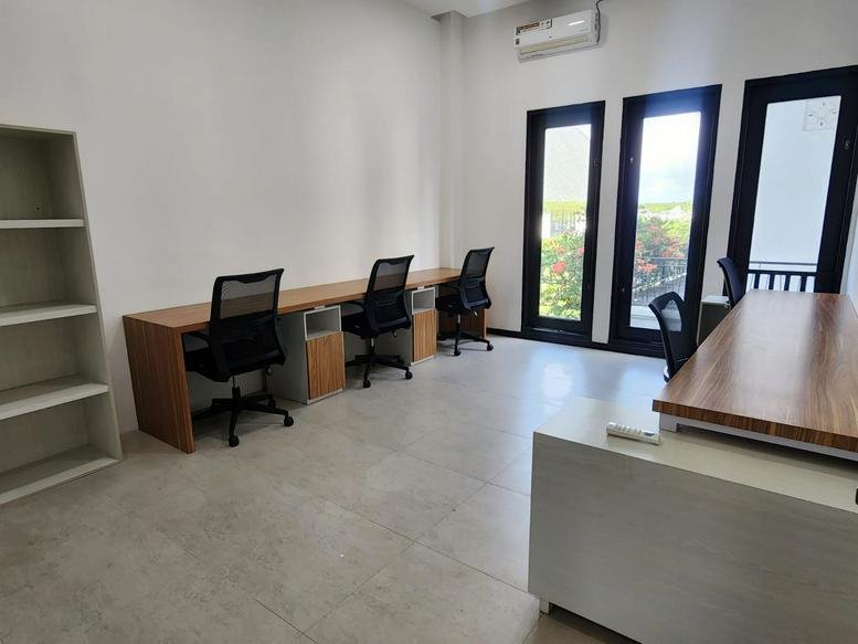 Spacious three-person workspace at 602, Jalan Bypass Ngurah Rai, Denpasar with wood-tone desks and floor-to-ceiling windows.