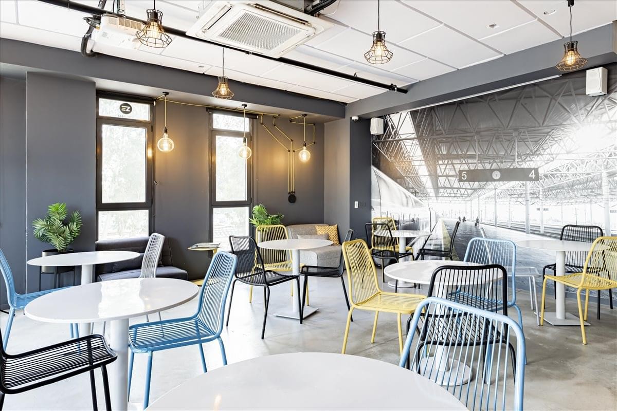 Spacious communal cafe area at Easyspace Binyamina with colorful seating and industrial lighting.