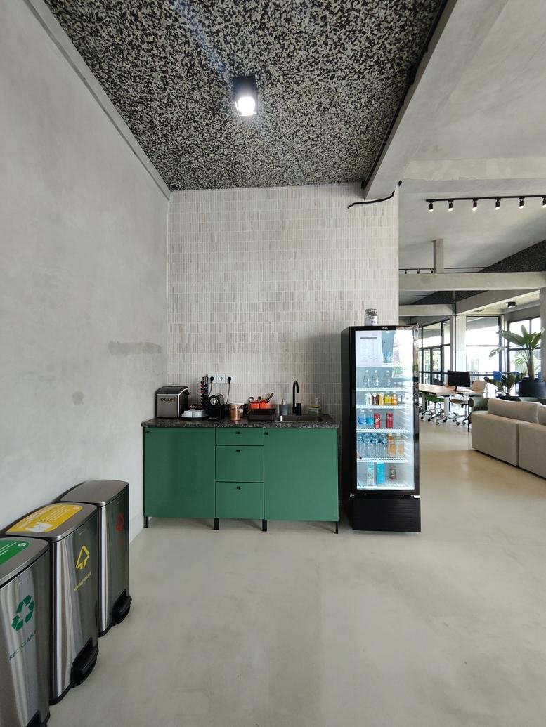Kitchenette area with green cabinetry, a black beverage fridge, and recycling bins.