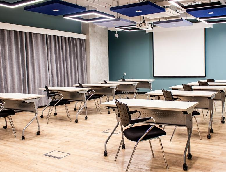 Bright training room at Armstrong Corporate Center with rows of white desks, black chairs, and a projector screen.