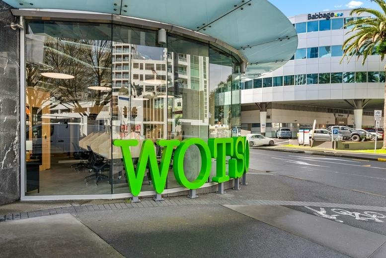 Exterior entrance of the building featuring curved glass windows and green signage.