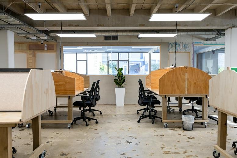 Coworking space with wooden privacy carrels, ergonomic black chairs, and large windows.