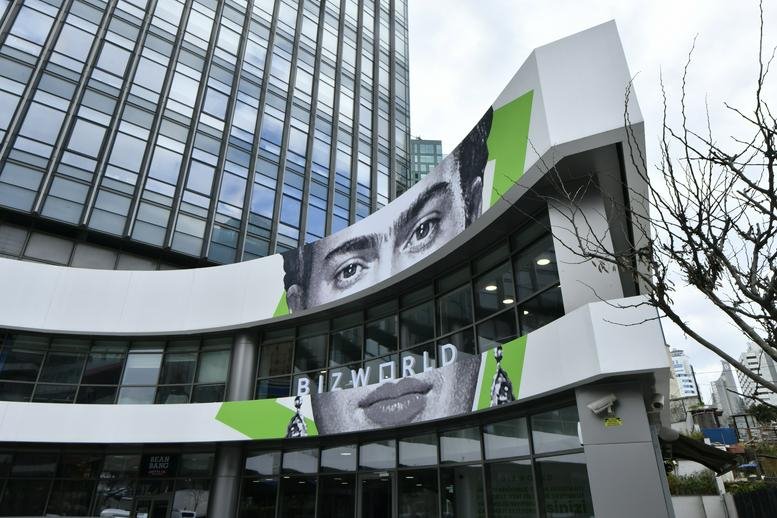 Modern exterior facade of Olive Plaza featuring a curved glass front and large monochrome artistic portrait.