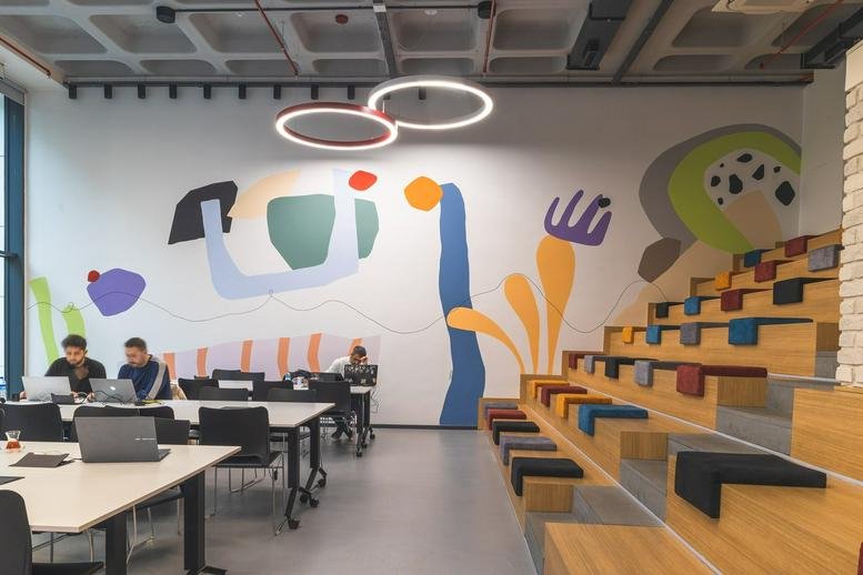 Spacious coworking area at İzQ Girişimcilik Merkezi with mural, tiered seating, and modern pendant lights.