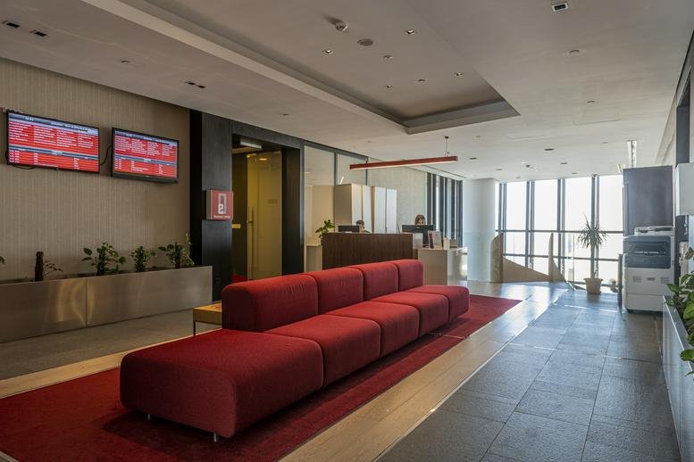 Spacious reception area with red seating and digital screens.