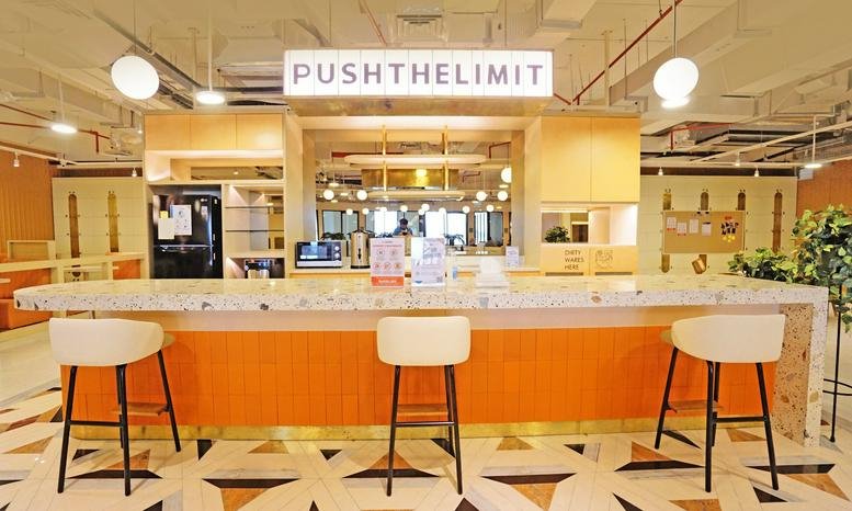 Cafe-style breakout area at Arkadia Green Park, Tower G featuring an orange bar and white stools.