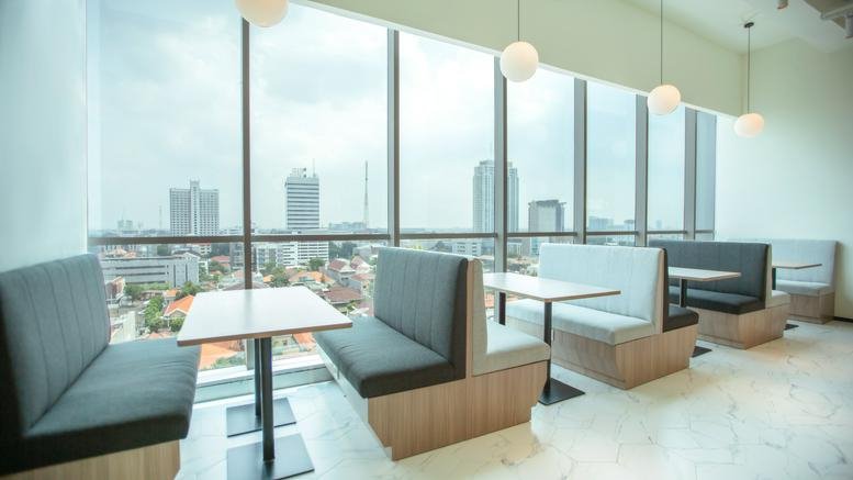 Sunny dining booths and tables at BEI Surabaya by large floor-to-ceiling windows with city views.