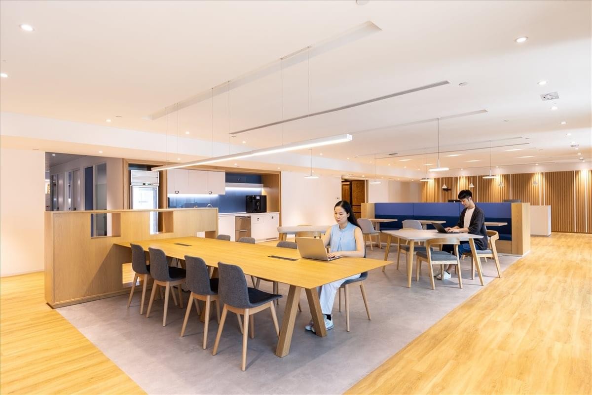 Contemporary coworking space with a long wooden communal table and lounge seating.
