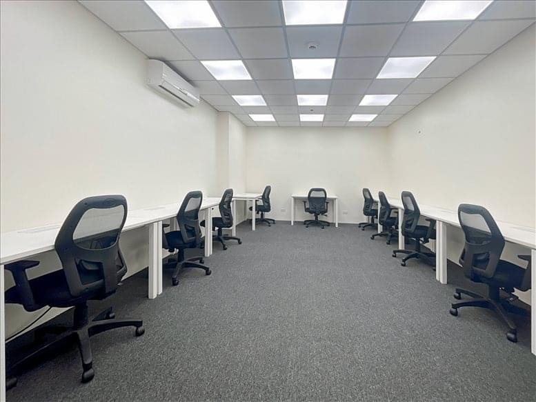 Spacious office suite with white workbenches, black ergonomic chairs, and grey carpeting.