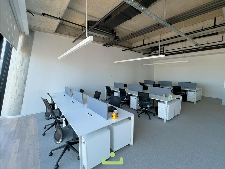Spacious open-plan office with rows of white desks and ergonomic black chairs.