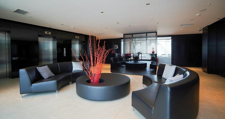Spacious reception lounge at Exen Residence featuring black curved sofas and a vibrant red branch center-piece.