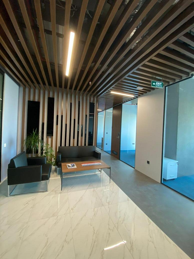 Bright lounge area with wood-slat ceilings, black leather sofas, and marble-style flooring.