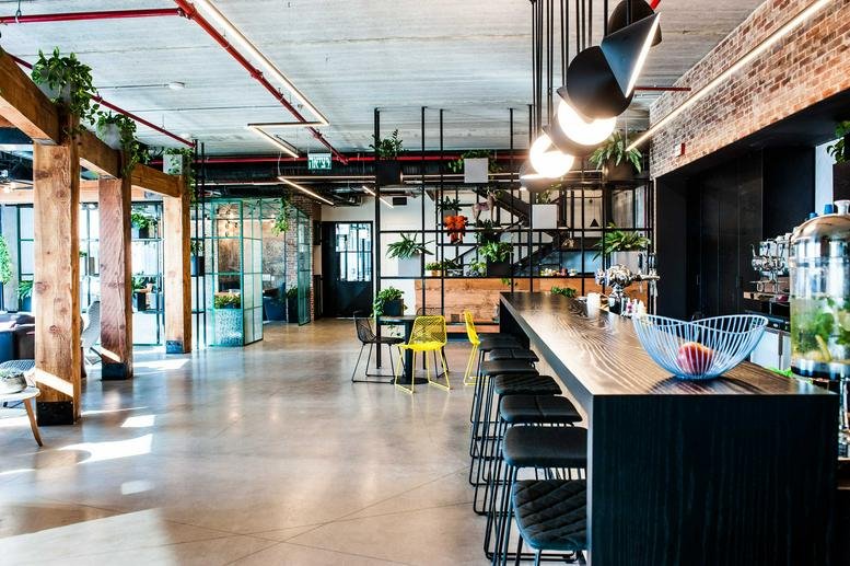Spacious communal lounge at Hashahar Tower with a long bar, wooden accents, and hanging plants.