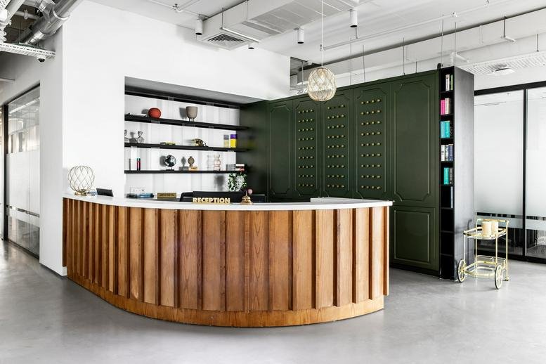 Reception area at Hachsharat Hayeshuv Tower with a curved wood-slat desk and dark green storage wall.