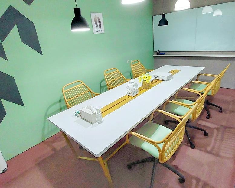 Breakout area with a long white table, woven chairs, and a green wall with geometric patterns.