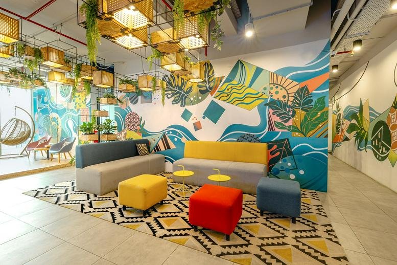 Colorful lounge area with modular sofas, bright ottomans, and a large tropical-themed wall mural.