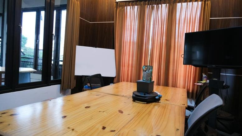 Private meeting room featuring a wooden table, orange curtains, and a television monitor.