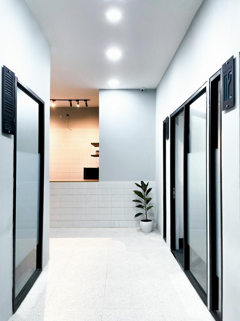 Brightly lit minimalist corridor at Jl. Trunojoyo No. 11 with glass doors and a potted plant.