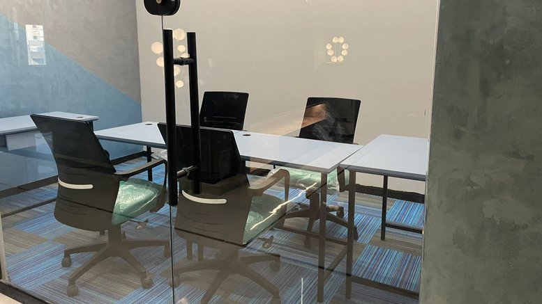 Internal view of a glass-walled private office at Karam Tower featuring ergonomic chairs and blue striped carpet.