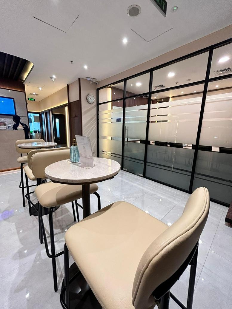 Common area at Kav. 28, Jalan Letjen S. Parman, Jakarta featuring tall cafe tables and frosted glass walls.