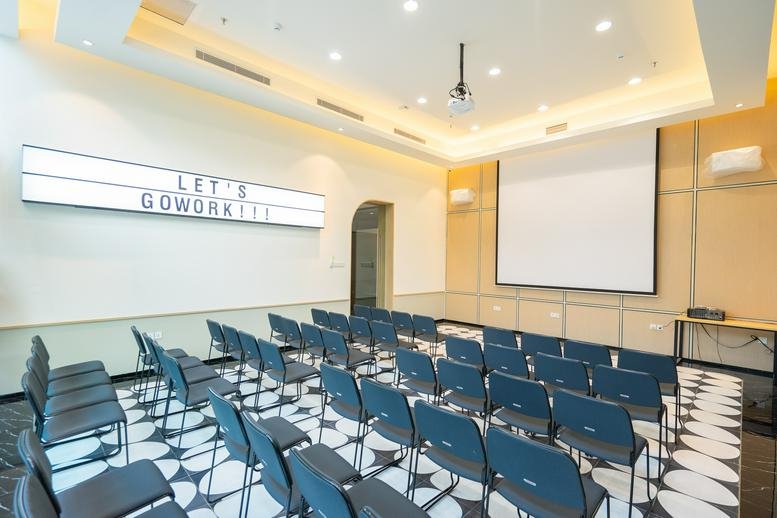 Spacious auditorium-style meeting room at Lippo Mall Puri with rows of blue chairs and a large projector screen.