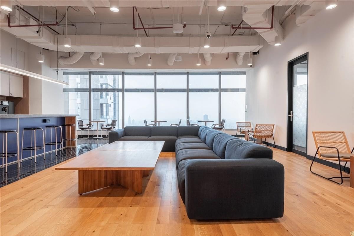 Bright communal lounge featuring a long black sectional sofa and warm wood flooring.