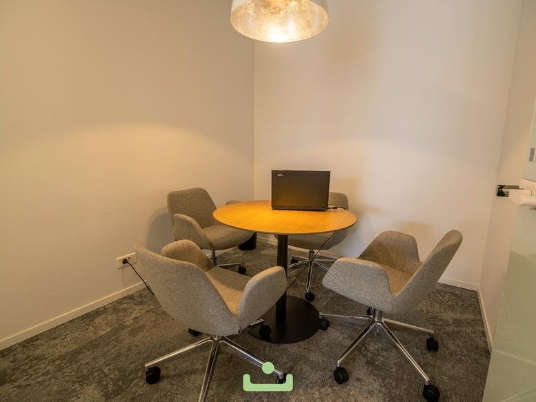 Small meeting room with a round wooden table, four grey chairs, and a silver pendant light.