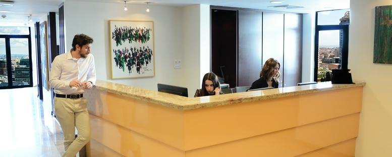 Modern light-wood reception desk staffed by professionals in a bright, open lobby area.
