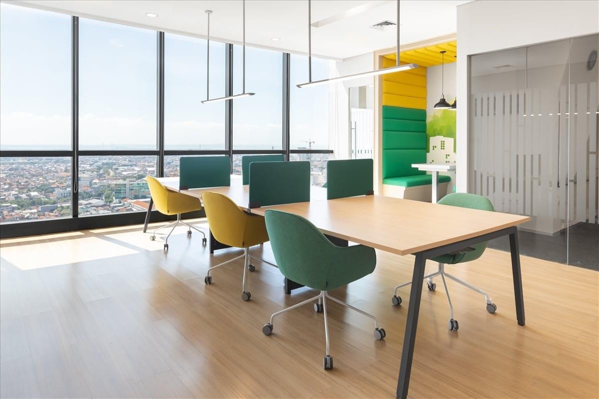 Sunlit coworking area with large windows offering expansive city views and colorful seating.