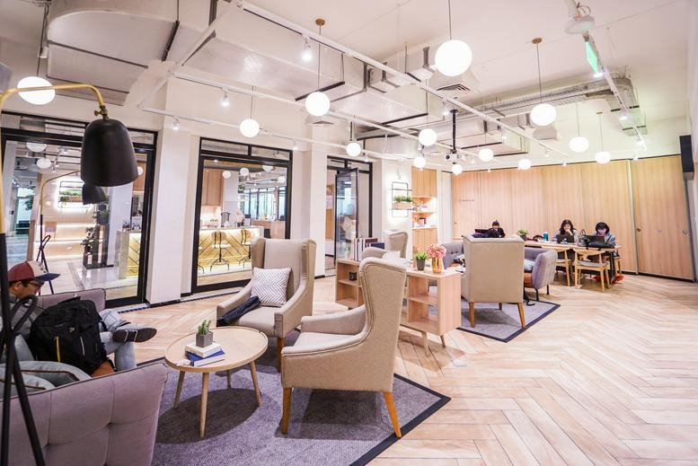 Spacious coworking lounge with comfortable armchairs, a coffee table, and a chevron patterned wood floor.