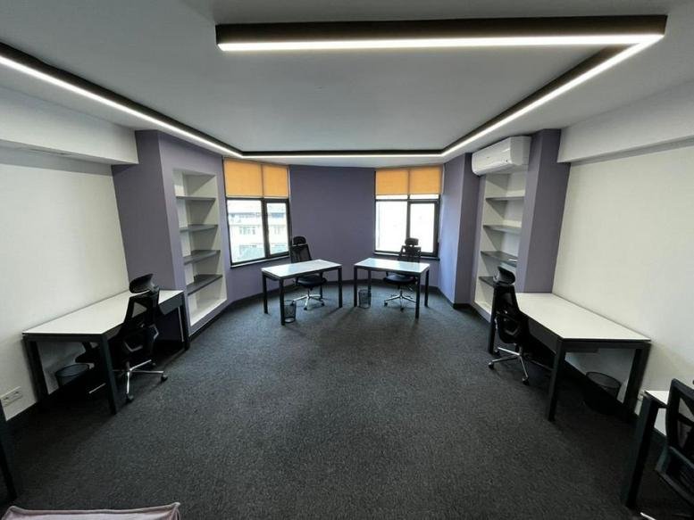 Wide-angle office space with multiple white desks, purple accent walls, and wrap-around LED lighting.