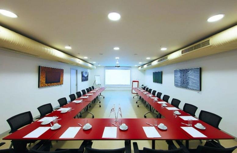 Spacious boardroom featuring a large U-shaped red table and white walls.