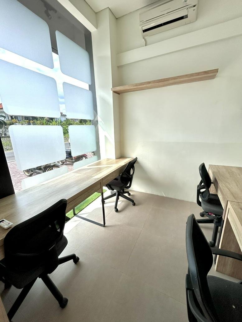 Bright shared workspace at Promenade Canggu with wooden desks facing a window.