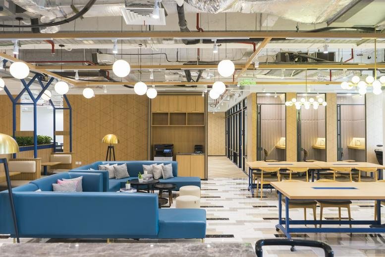Spacious communal lounge and coworking area at Sahid Sudirman Center with blue sofas and globe pendant lights.