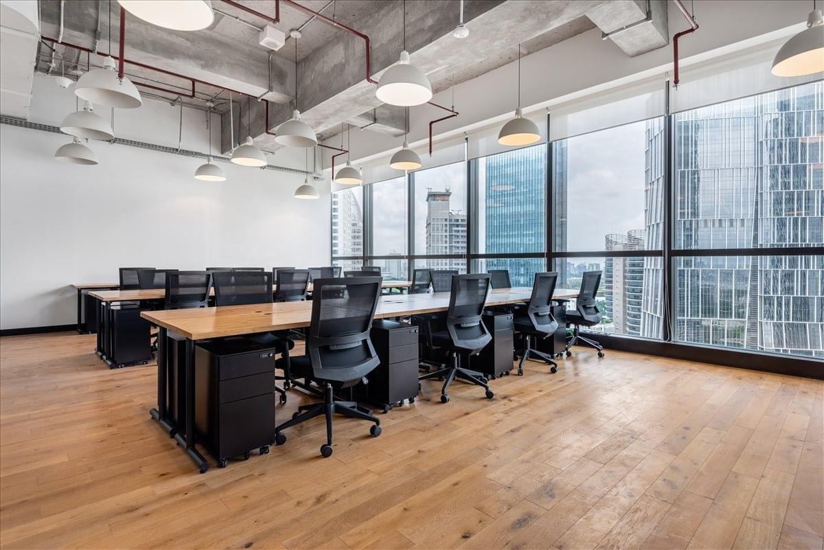 Spacious open-plan office with rows of wooden desks and floor-to-ceiling windows.