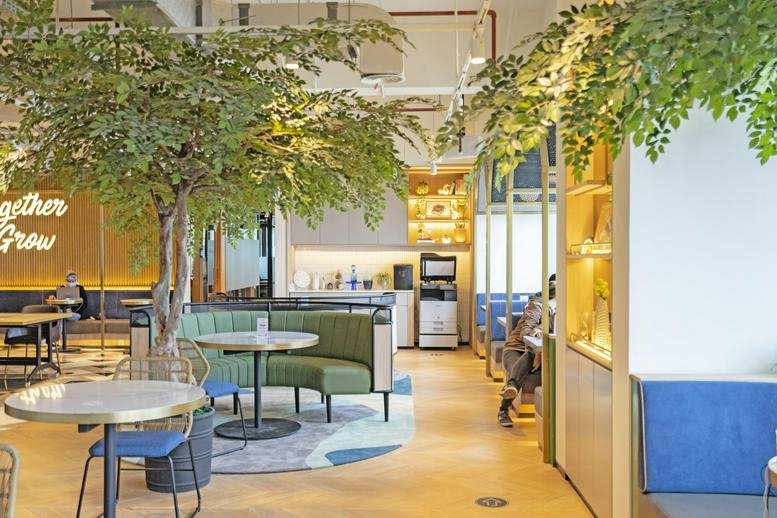 Spacious communal lounge at Sopo Del Tower B, 22nd Floor, with indoor trees, booth seating, and cafe tables.