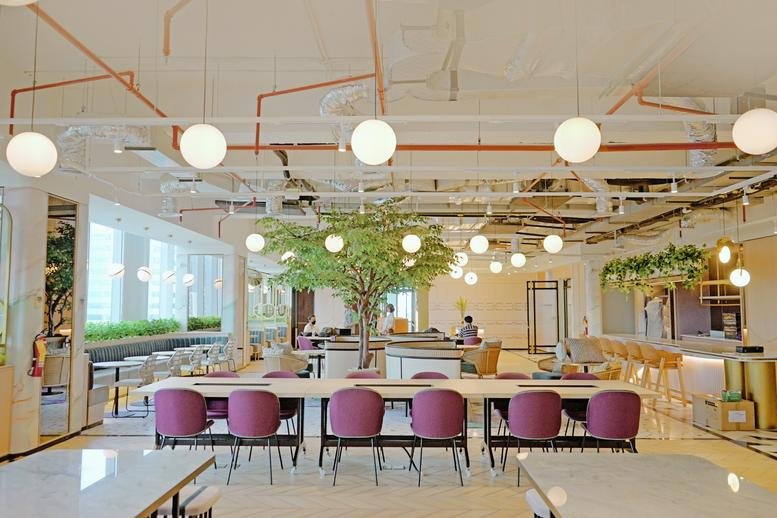 Spacious communal lounge at XL Axiata Tower with warm lighting, indoor trees, and colorful purple seating.