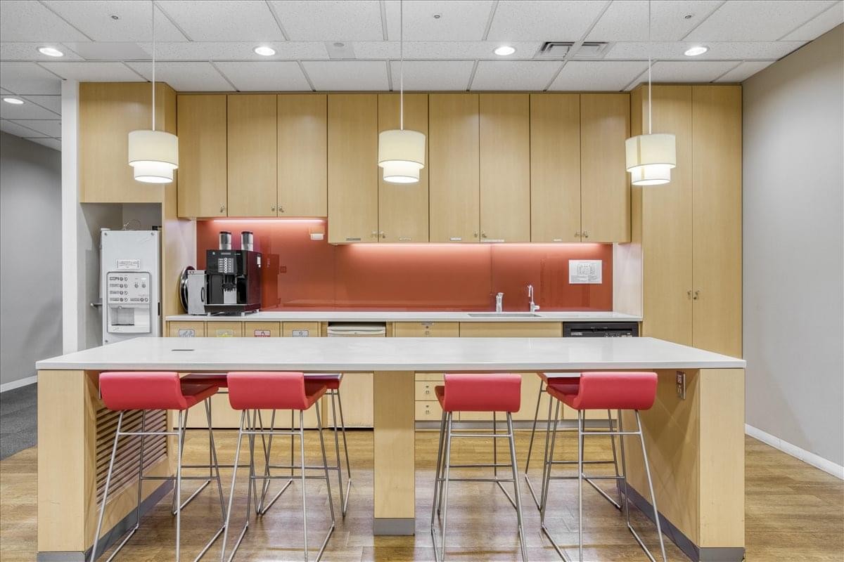Bright communal kitchen and breakout area with red stools and a long island bench.