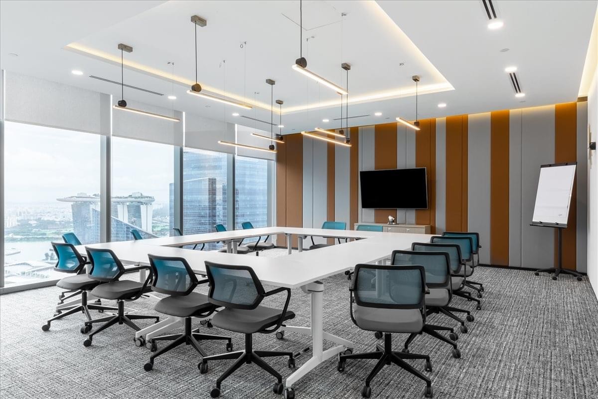 Spacious boardroom with a large white square table, blue ergonomic chairs, and designer pendant lighting.