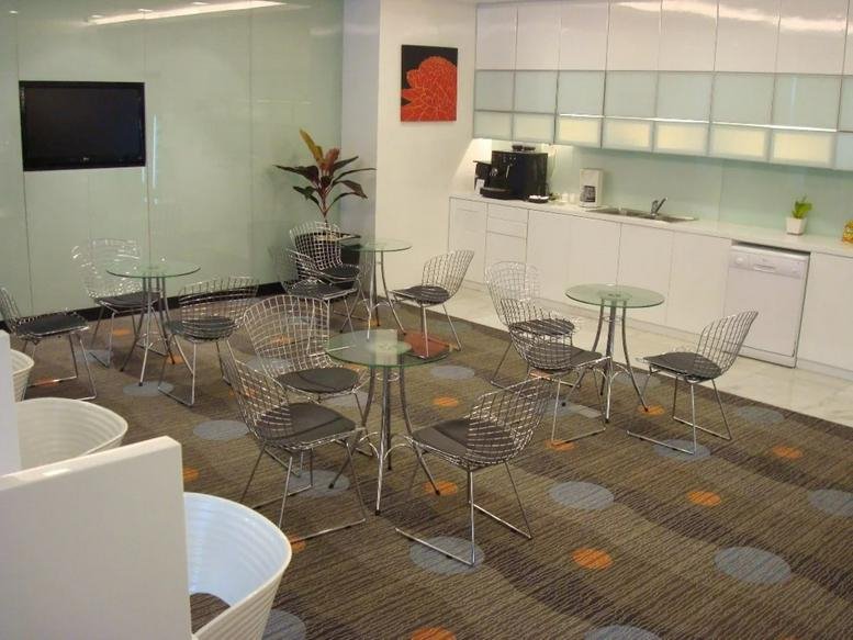 Communal break area with small café tables, chairs, and a kitchen unit at Athenee Tower.