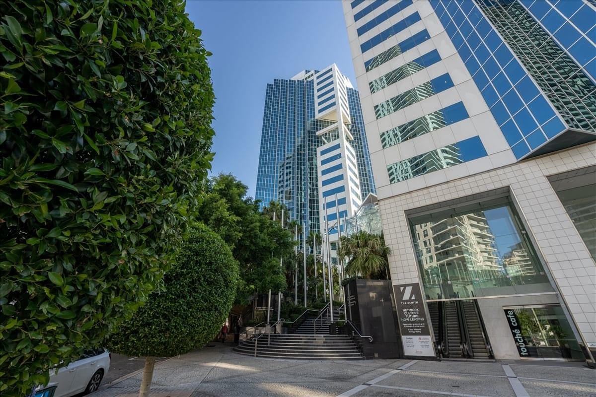 Exterior view of the glass-facade Zenith Centre, Chatswood Corporate Centre with lush green trees in the foreground.