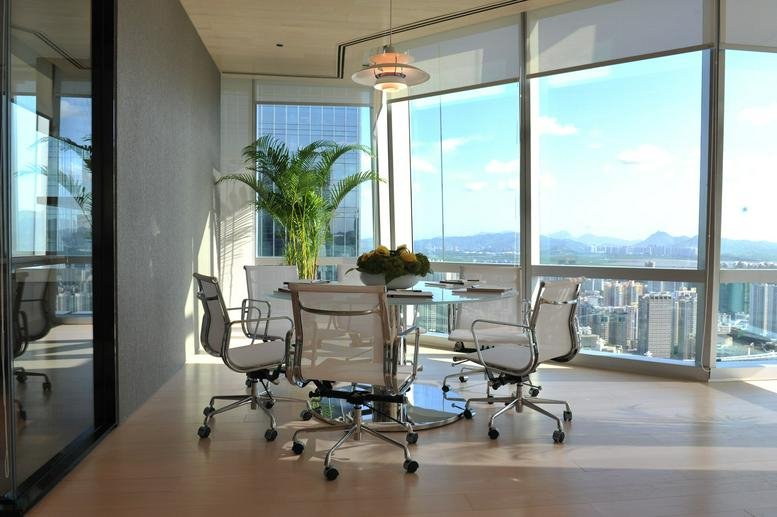 Sunlit communal breakout area with a dining table and potted plants overlooking the city.